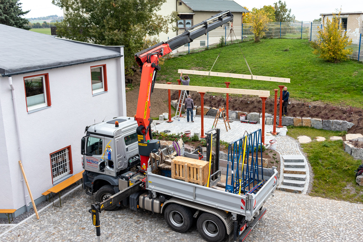 Die Pfetten sind ausgearbeitet und werden mit dem Kranarm auf die Säulen gehoben und vom Zimmerer befestigt.